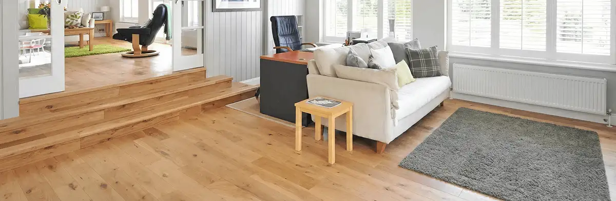 A modern living room with professionally installed laminate flooring, a beige sofa, a small side table, a gray rug, and large windows with white shutters in Salt Lake City, UT